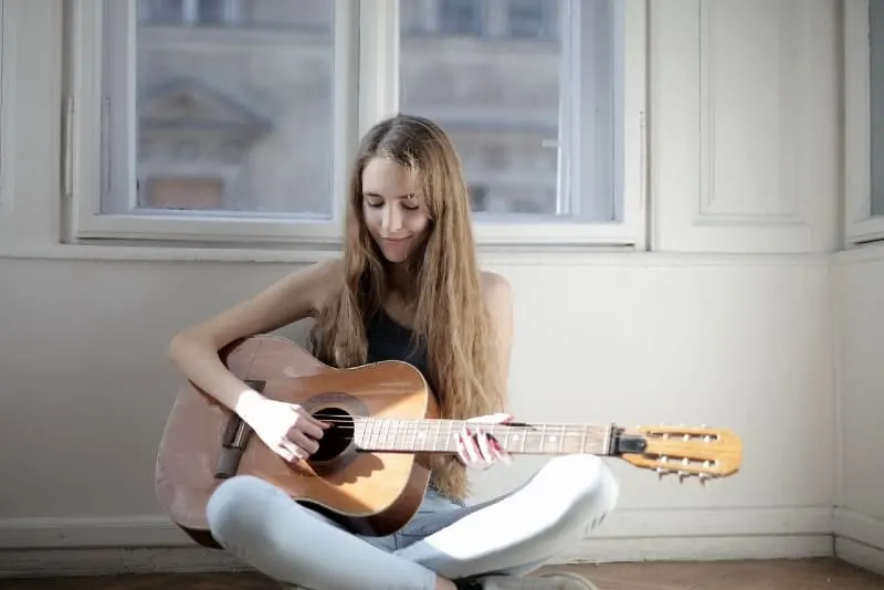 woman playing guitar while sitting on floor near window
