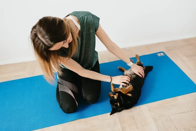 woman playing with a little puppy in a blue yoga mat