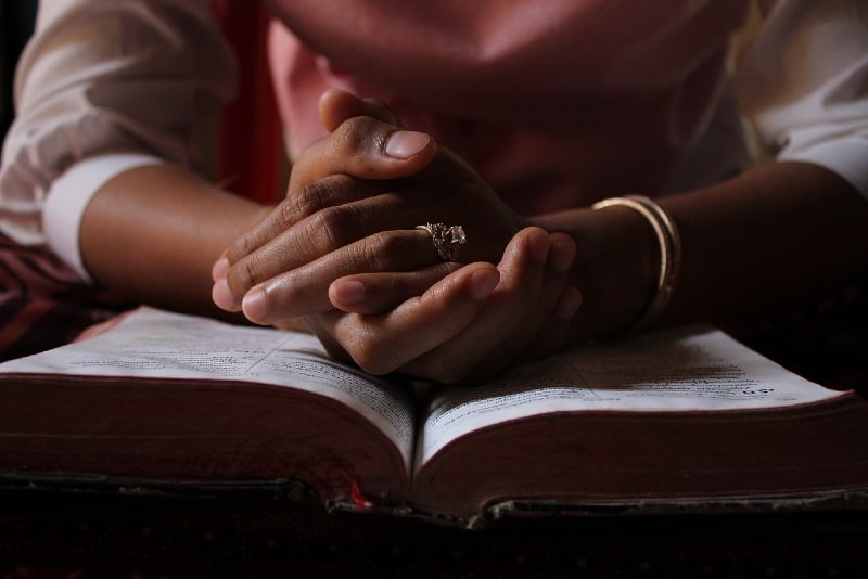 woman praying while leaning hands on bible