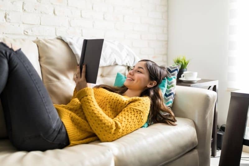 mujer leyendo un libro tumbada en el sofá dentro de casa
