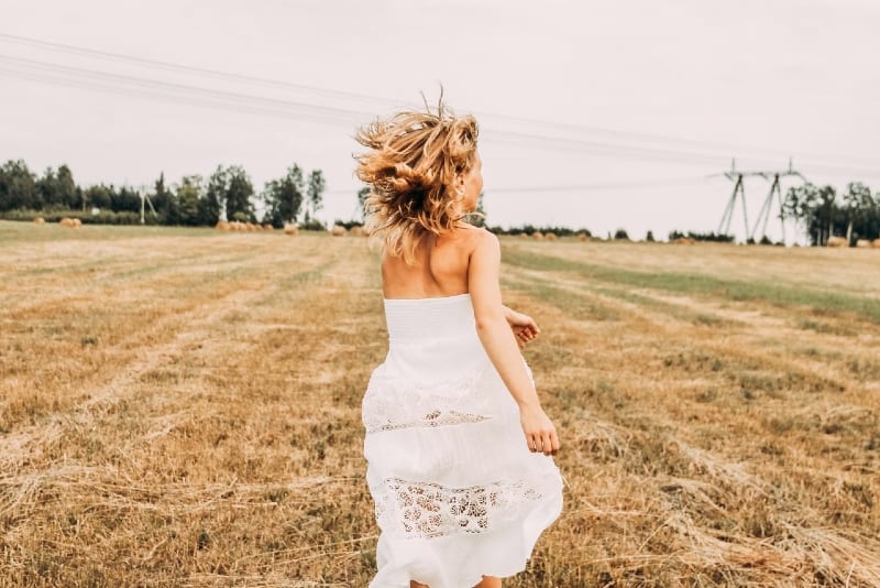 mujer con vestido blanco corriendo en un campo de hierba marrón