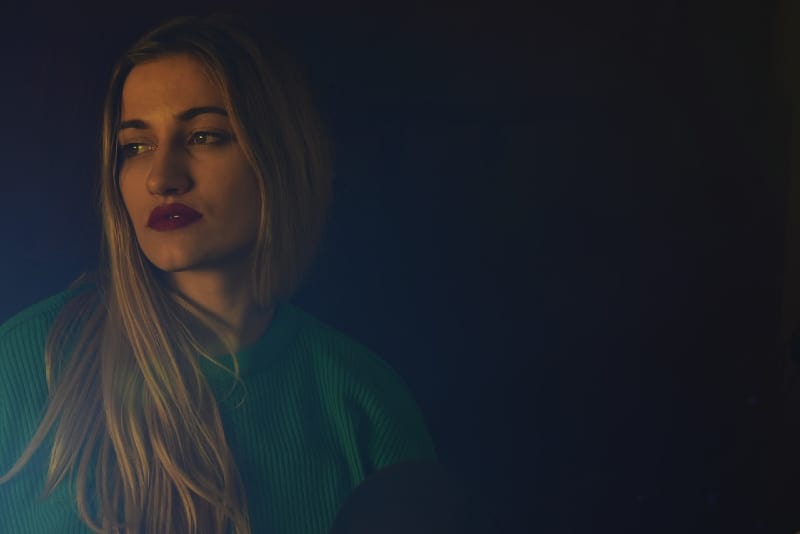 blonde woman in green sweater sitting near wall