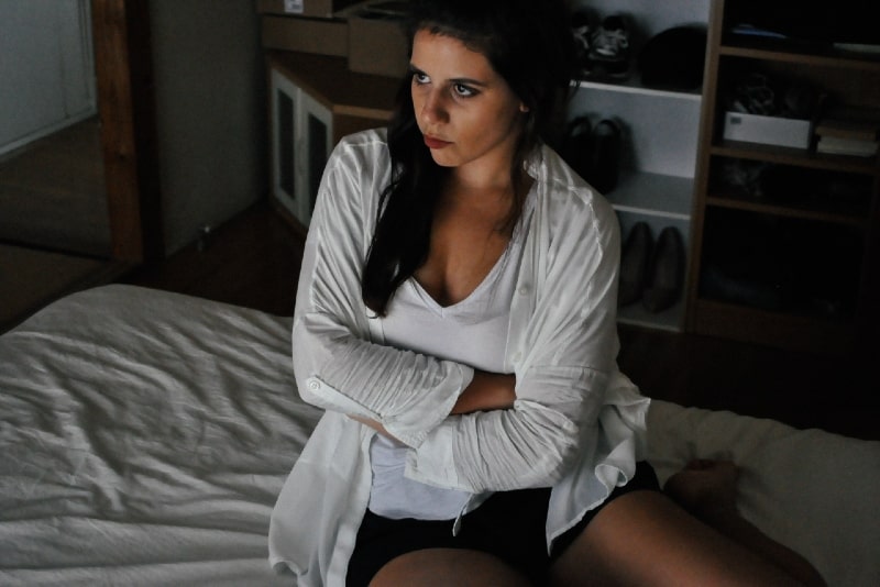 sad woman in white cardigan sitting on bed