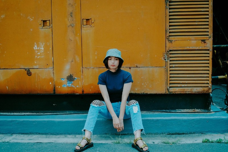 woman with bucket hat sitting on concrete surface