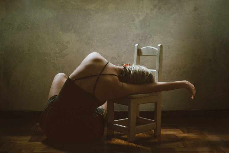 donna seduta sul pavimento appoggiata a una sedia