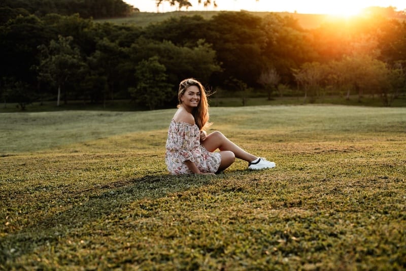 mulher sorridente com vestido floral sentada na relva