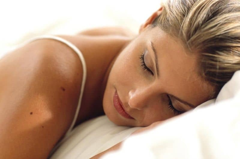 mujer durmiendo en cama con sábanas blancas 