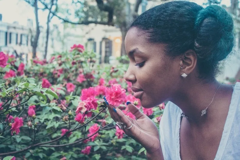 woman with earrings smelling pink flower