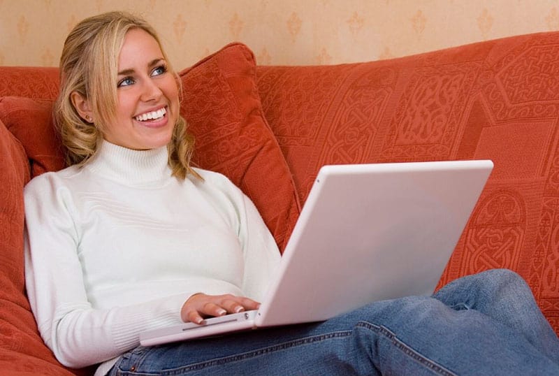 woman smiling while working from home sitting at the couch working on laptop
