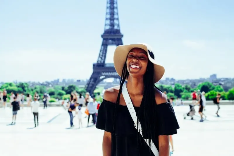 smiling woman with hat standing behind eiffel tower