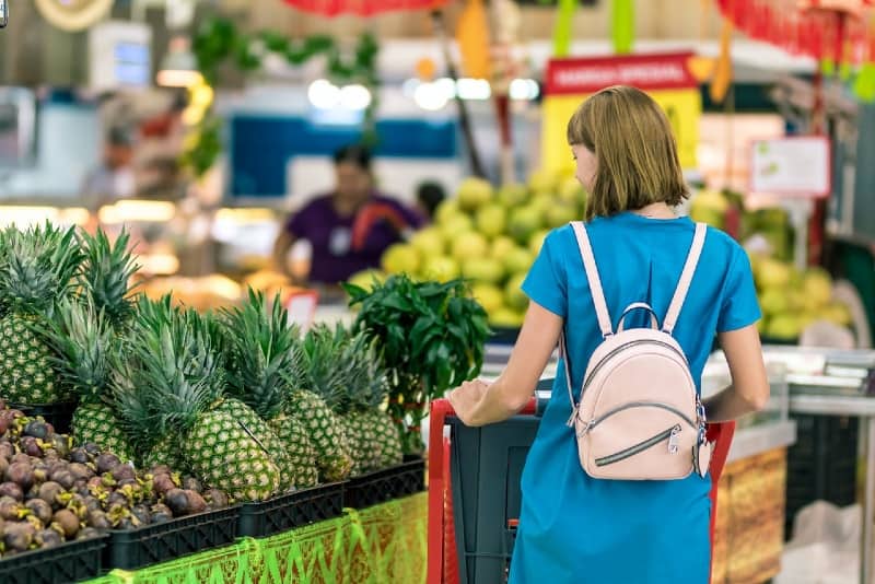 mujer con mochila blanca de pie junto a piñas