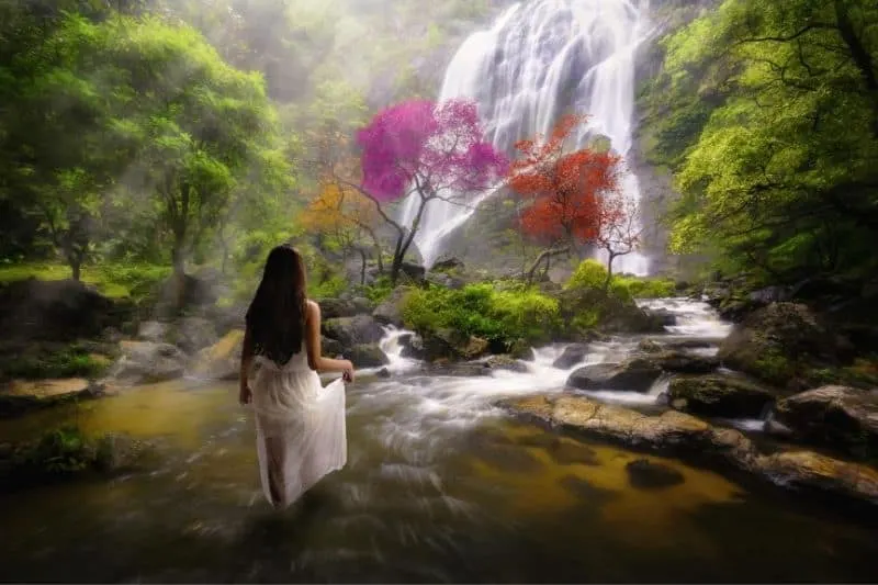 woman standing in the water near the waterfalls in the dreamy forest