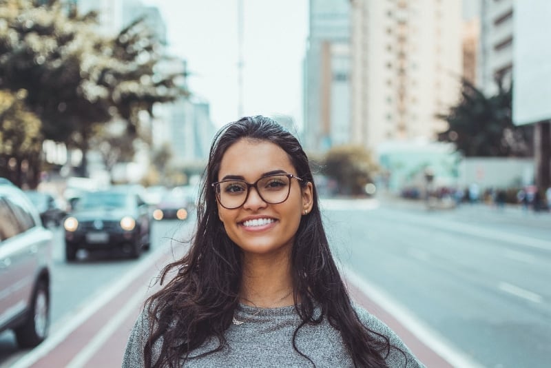 smiling woman with eyeglasses standing near road