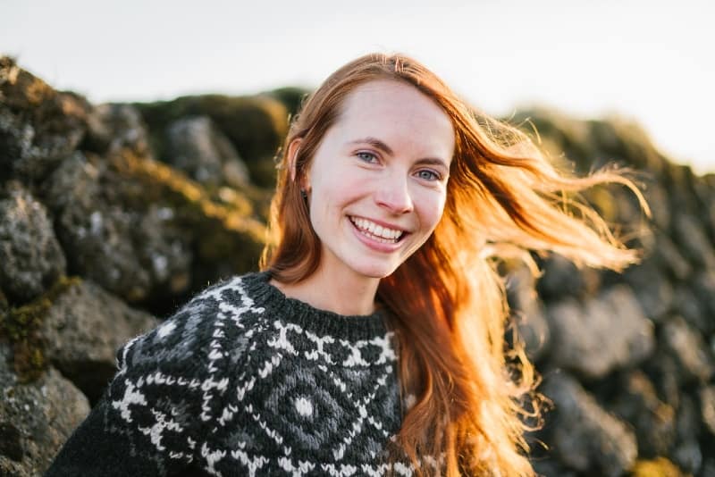 mulher ruiva sorridente junto a um muro de pedra