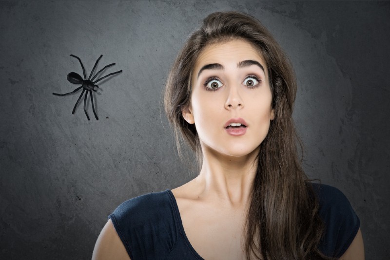 scared woman standing near wall with spider