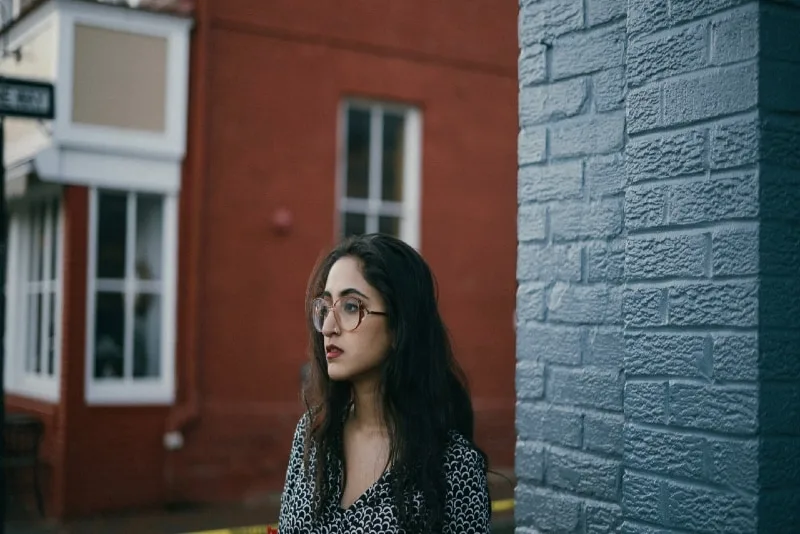 woman with eyeglasses standing near brick wall