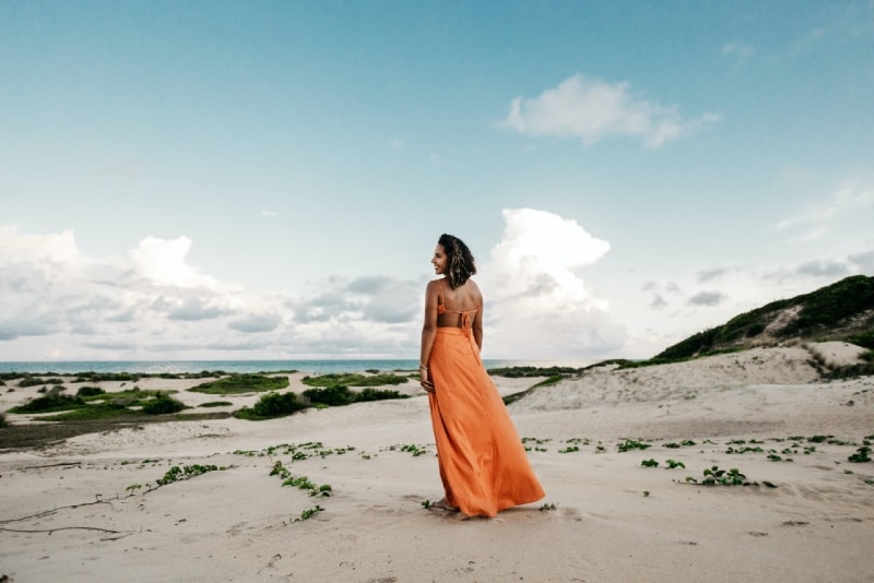 donna sorridente in abito arancione in piedi sulla spiaggia