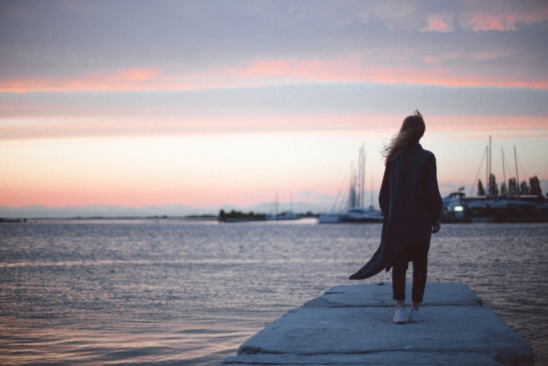 mujer de pie en el muelle durante la puesta de sol