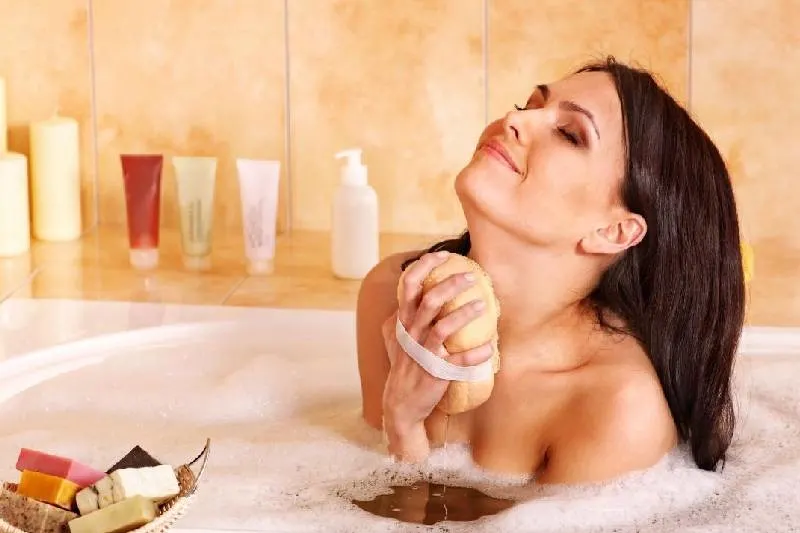 woman taking a bubble bath in a bath tub rubbing with sponge happily