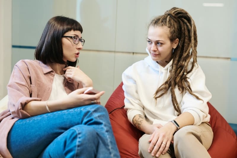 donna che parla con una donna mentre è seduta su una borsa per pigrizia