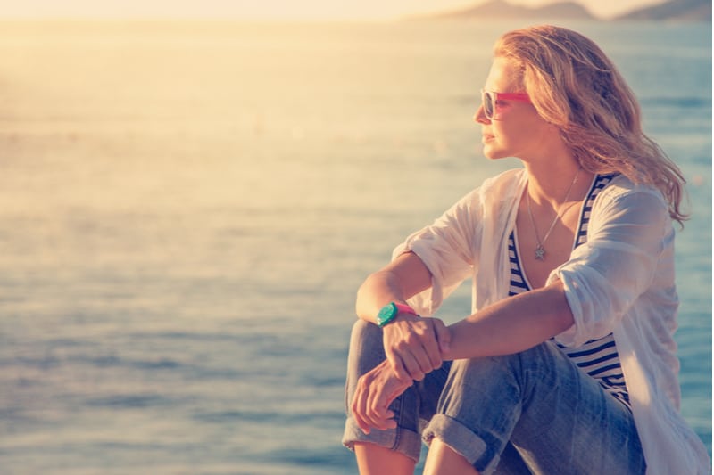 woman thinking near the sea sitting by the side wearing sunglasses