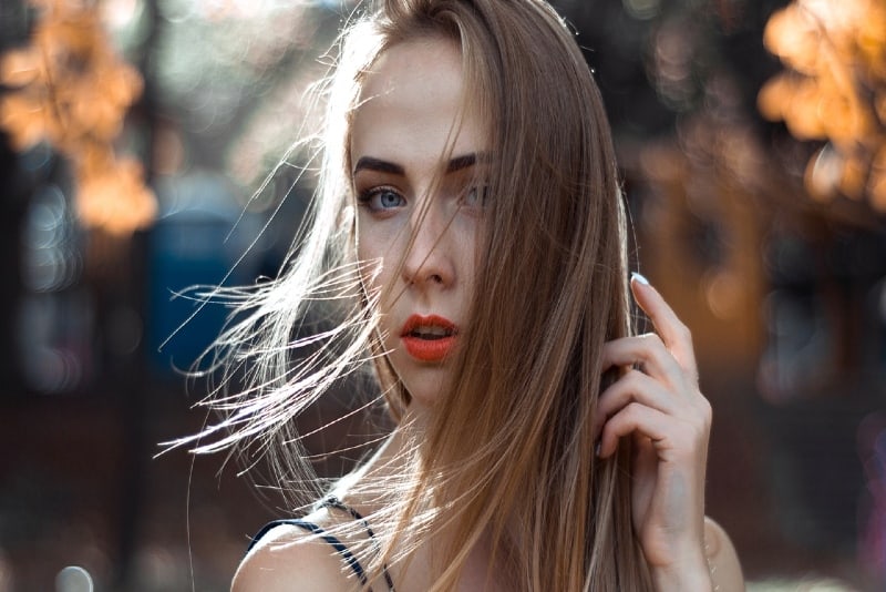 mujer con pintalabios naranja tocándose el pelo