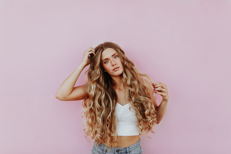 woman touching her hair while standing near pink wall