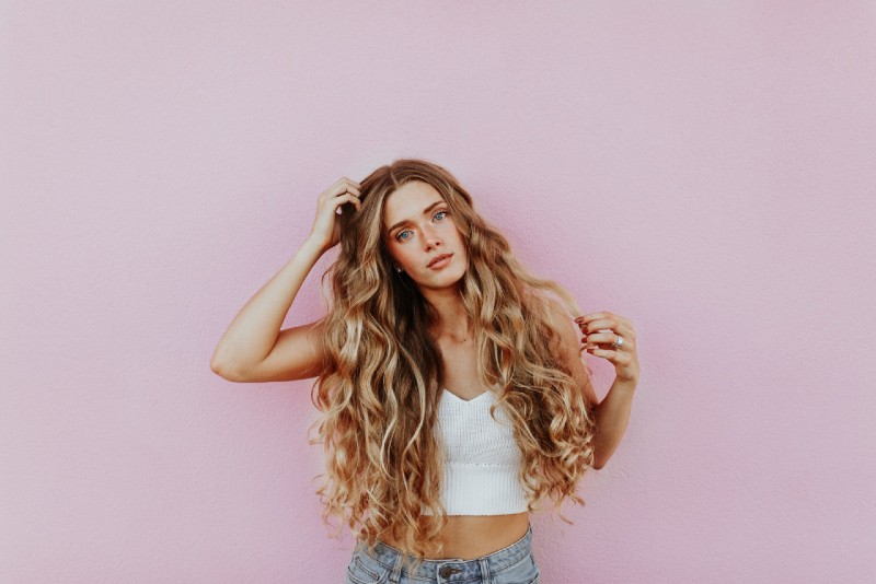 mujer tocándose el pelo cerca de una pared rosa