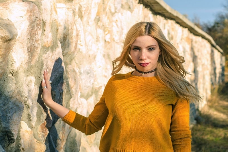 mujer con jersey amarillo tocando pared al aire libre