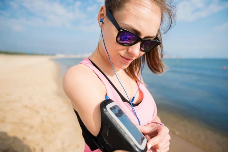 mujer encendiendo su lista de reproducción en su smartphone colocado en sus brazos lista para hacer footing