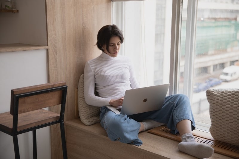 woman using laptop while sitting near window