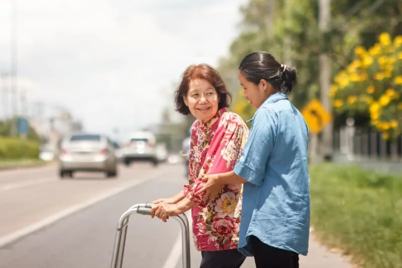 smiling woman using walker while looking at young woman