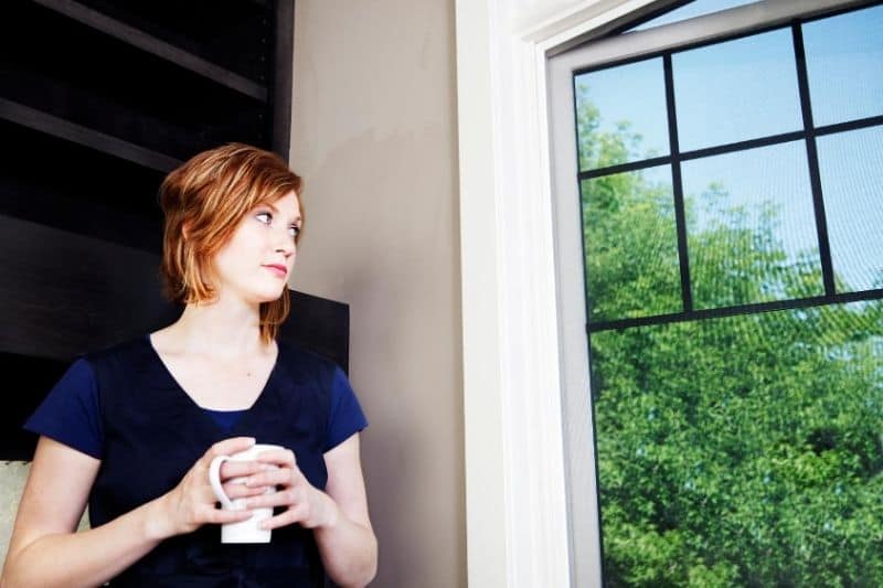 woman waiting cradles her mug standing near the big glass windows