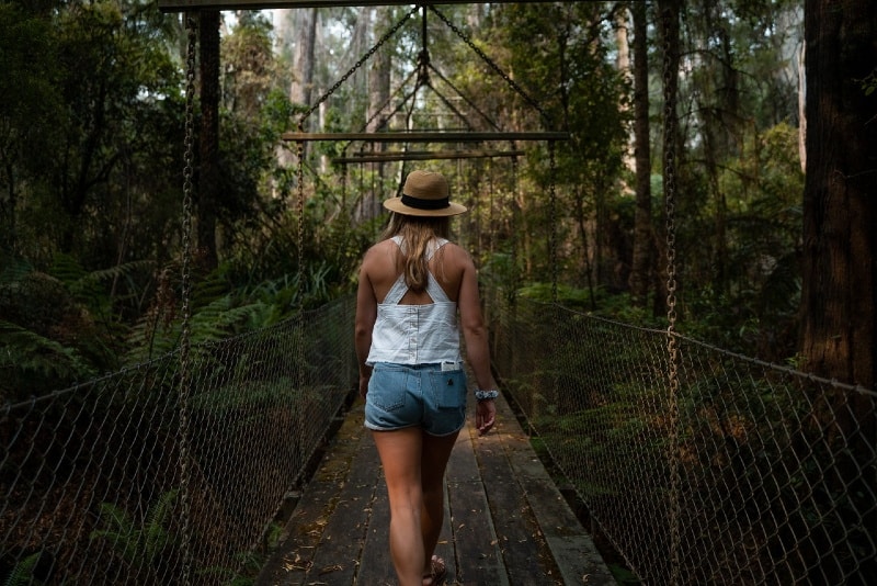 mujer con sombrero caminando por un puente