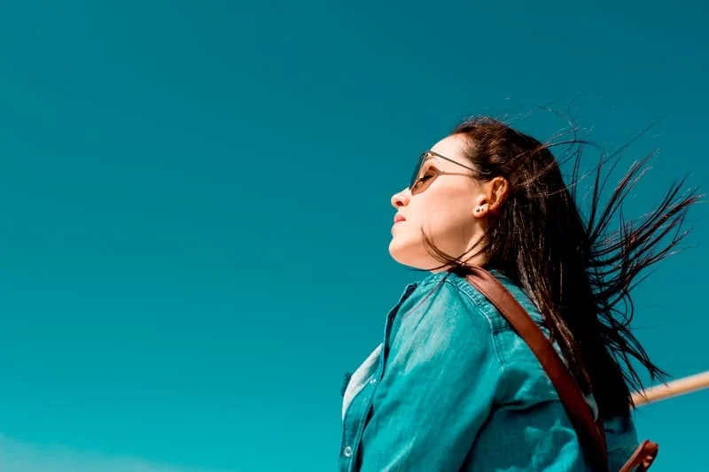 woman wearing shades closing her eyes wearing aquamarine blue top with sky of the same hue