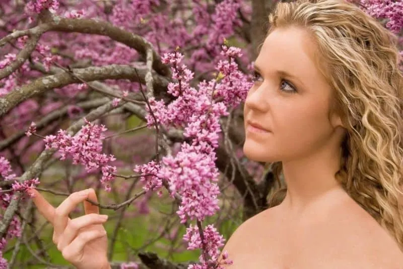 woman with innocent face standing against a tree with pink flowers