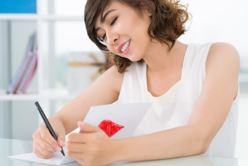 mujer sonriente con top blanco escribiendo en un papel