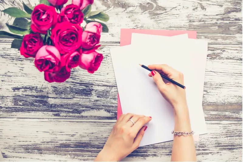 main de femme écrivant une lettre sur la table avec vase de roses rouges