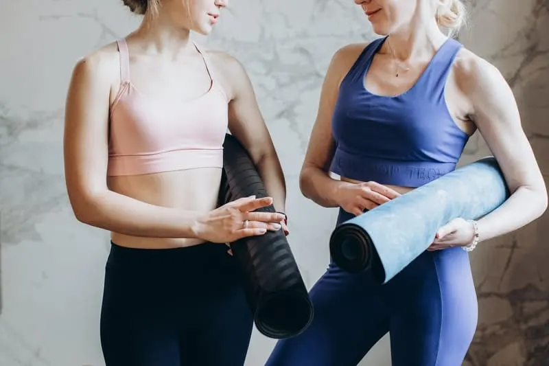 women bringing yoga mat wearing athletic wear chatting