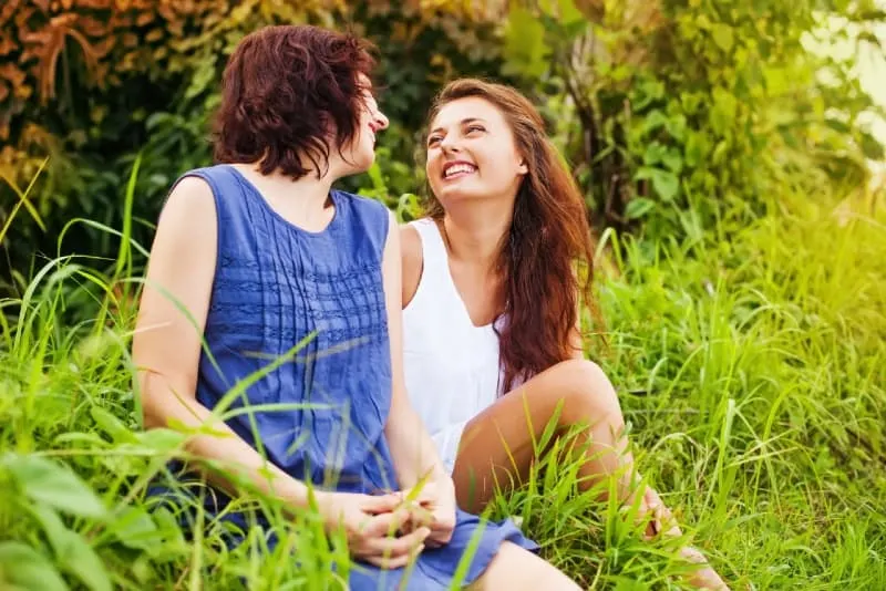 two women sitting on grass and laughing