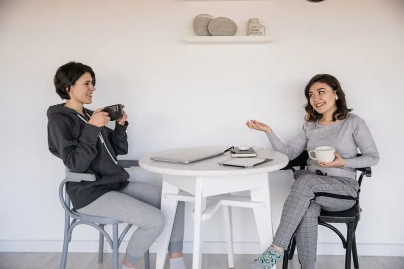 women talking to each other over a cup of coffee with a white table in between them