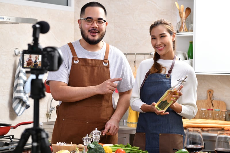 joven pareja asiatica vlogger grabando video dentro de la cocina sosteniendo aceite