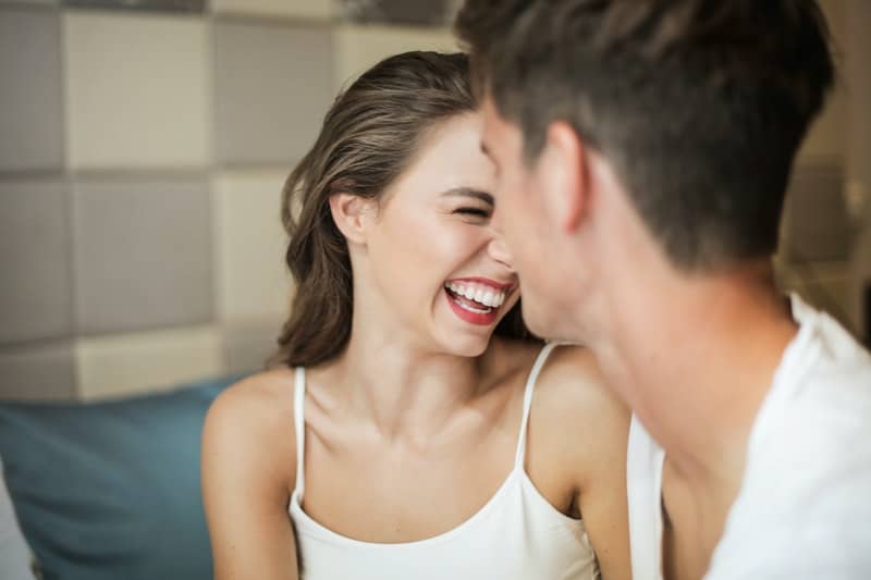 joven pareja riendo felizmente en el interior del dormitorio con top blanco