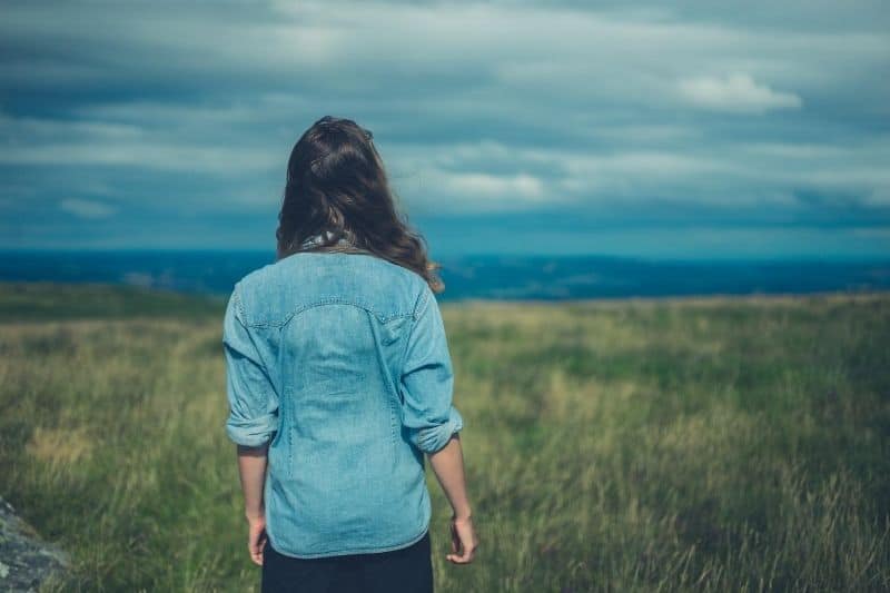 young lady standing in the meadows facing a blue sky covering the mountains