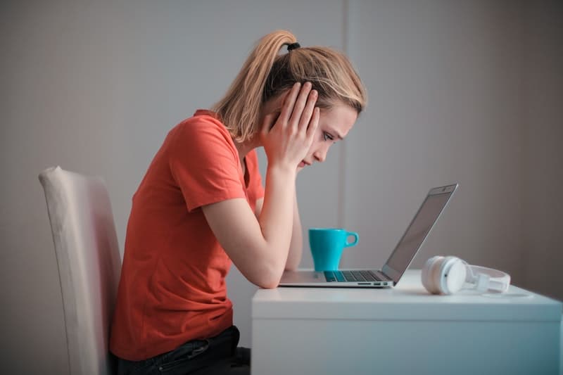 mulher jovem virada para o computador portátil a pensar profundamente com as duas mãos nas bochechas