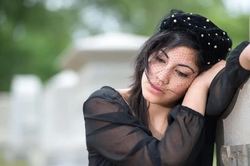 young woman mourns in the cemetery wearing black dress