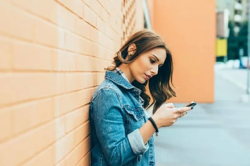 young woman outdoors using a smartphone while leaning on the wall