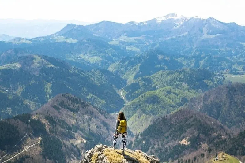 young woman stands in the mountain bringing a backpack