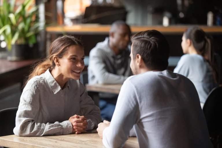 um homem e uma mulher a falarem com um sorriso enquanto se sentam à mesa