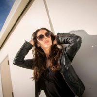 brunette woman wearing leather jacket and sun glasses standing outdoors